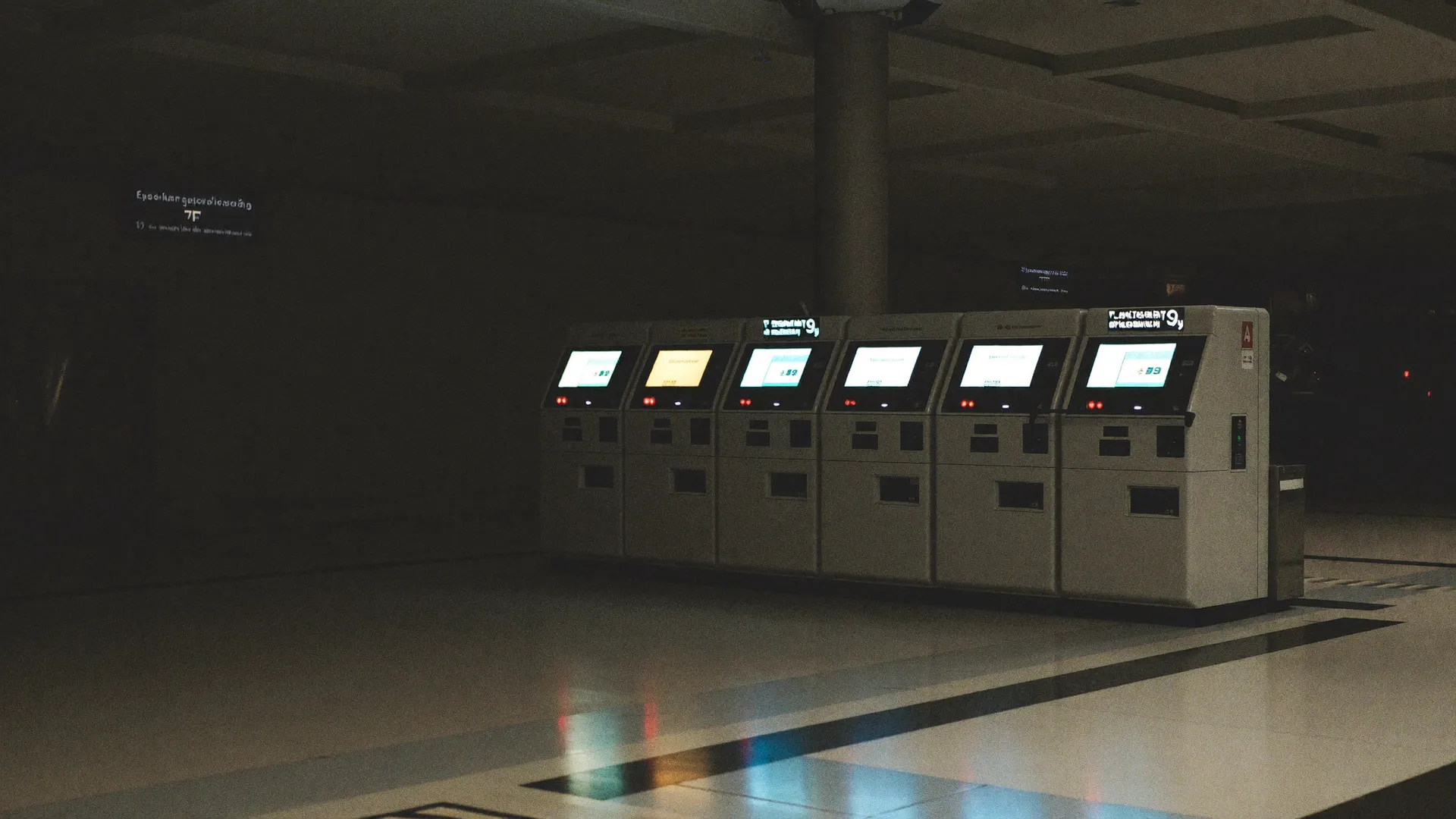 A row of ticket vending machines glowing in an empty station concourse at night