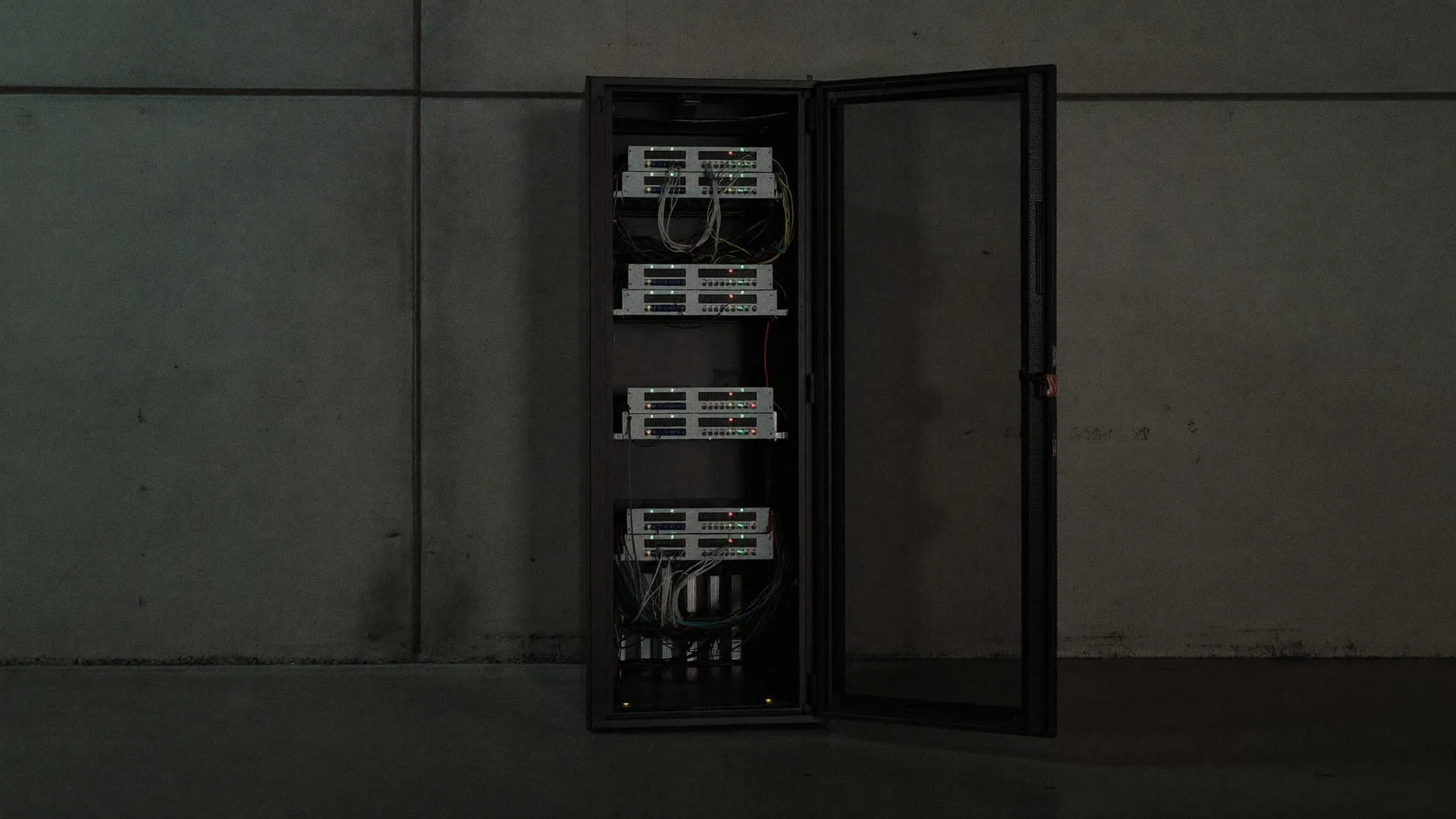 A single open server rack with glowing status lights against a concrete wall