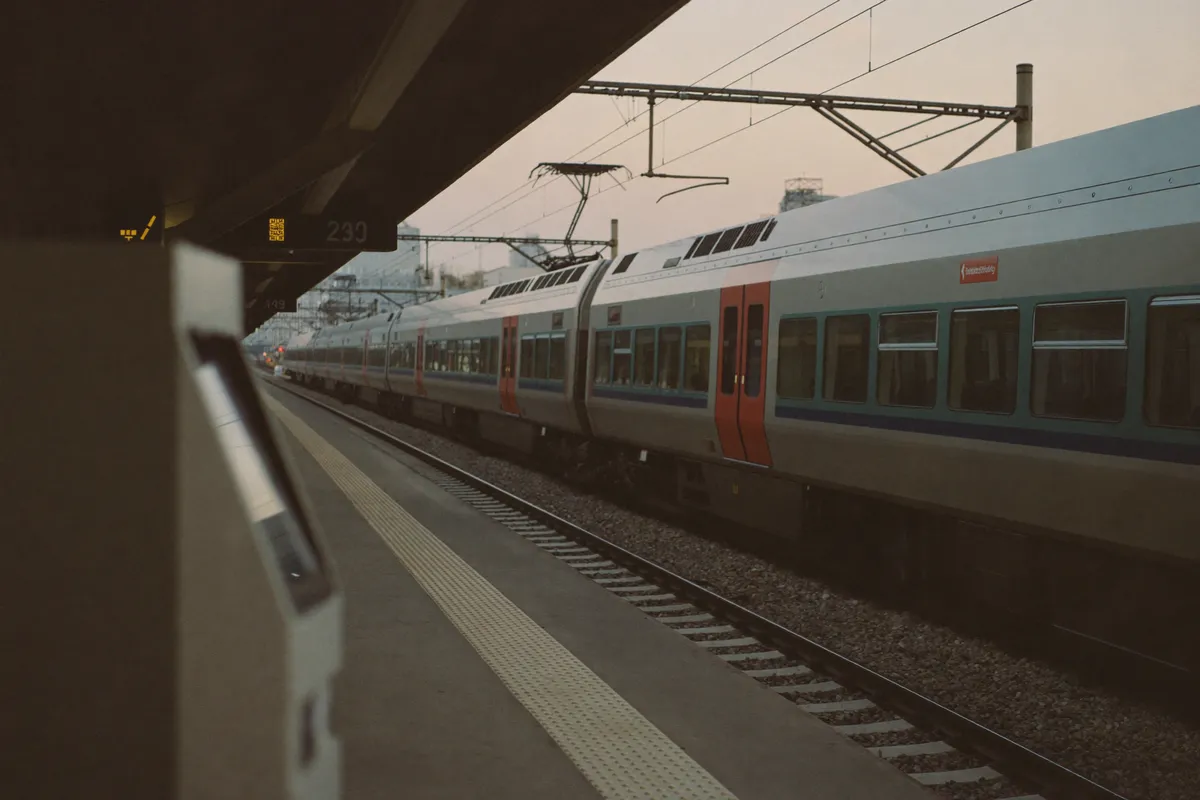 A regional train at a European station platform at dusk, a ticket machine in the foreground
